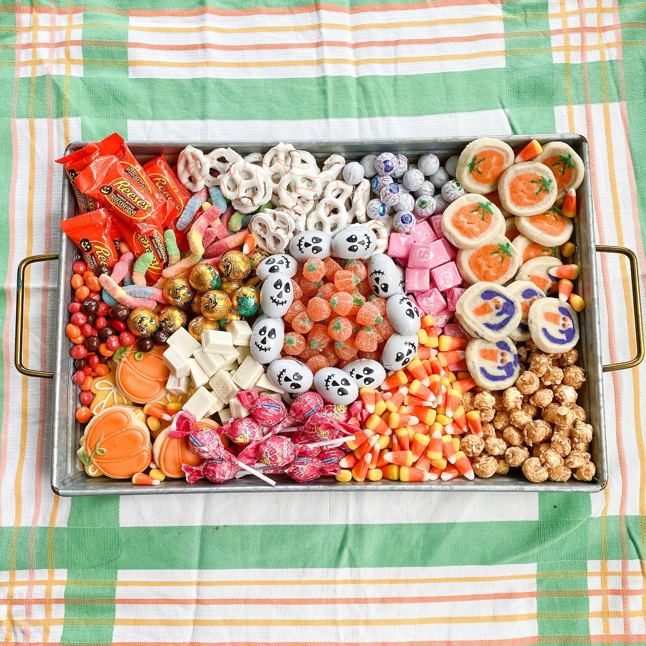 Metal tray filled with assorted Halloween candies and cookies on plaid tablecloth