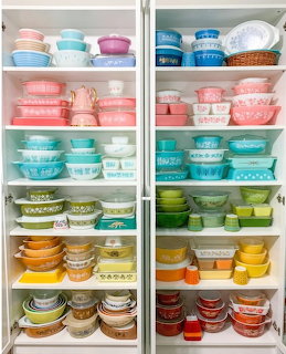 Organized cabinet shelves filled with colorful vintage Pyrex bowls and containers arranged by hue