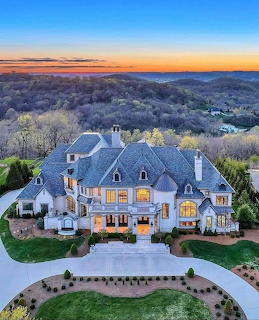 Aerial view of illuminated luxury mansion at sunset with landscaped grounds and hills