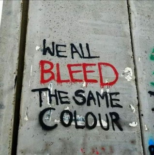 Graffiti stencil text reading 'We All Bleed The Same Colour' on concrete surface