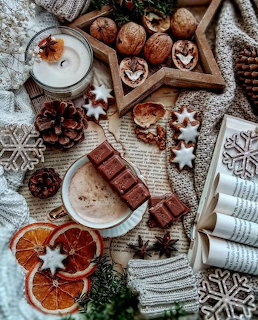 Overhead view of coffee, hot chocolate, chocolate treats, dried oranges, pine cones, and Christmas decorations on white knit fabric