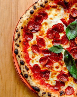 Pepperoni pizza with melted cheese, tomato sauce, and fresh basil on wood surface