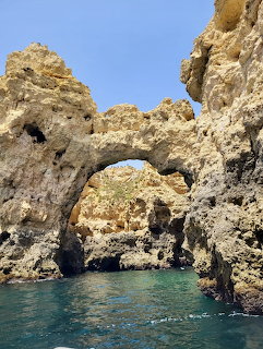 Natural stone arch in golden cliff face over turquoise sea water with blue sky