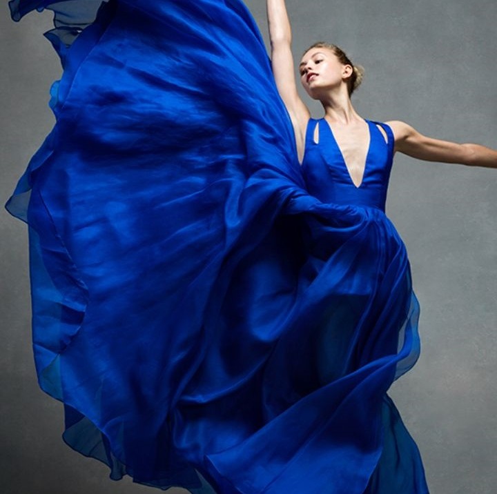 Ballet dancer in vibrant blue dress with fabric flowing upward in graceful motion against gray backdrop