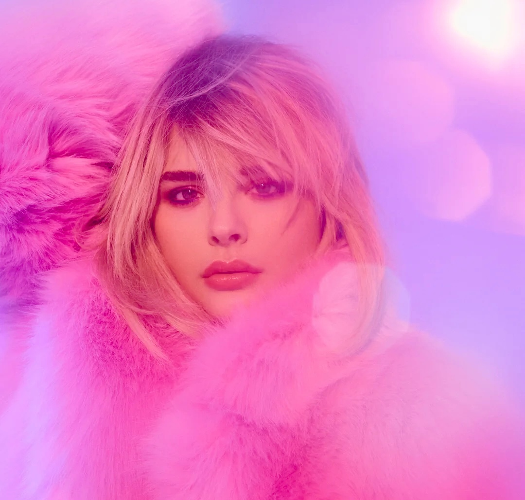 Blonde woman in pink fur coat against purple bokeh background