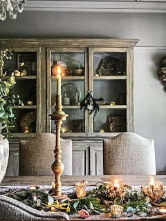 Rustic wooden hutch with dishes and decor, beige chairs, table with fall leaves and candles in elegant dining room