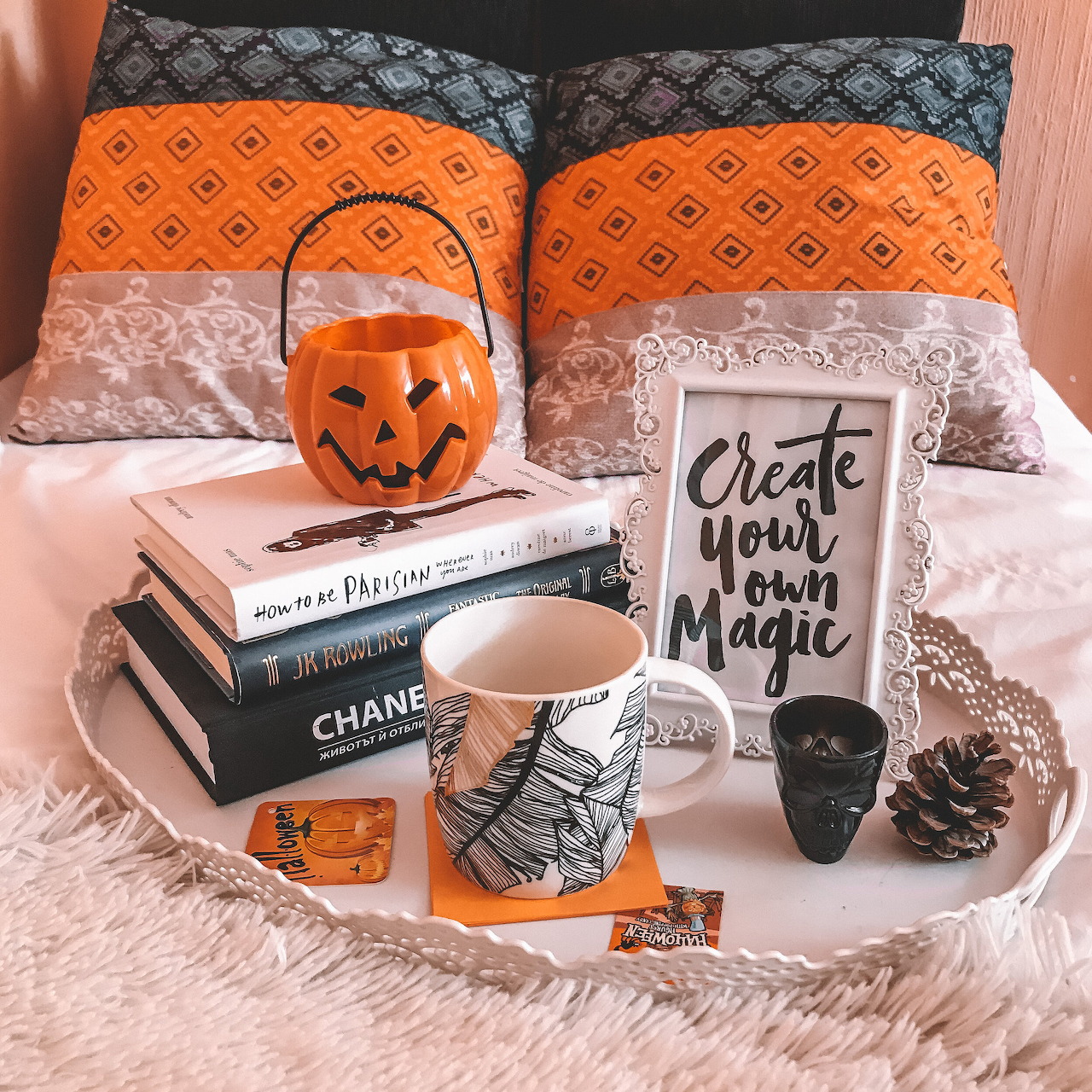 Halloween themed bedroom flatlay with orange pillows, books, decorative mugs, jack-o-lantern bucket, and cozy autumn decor