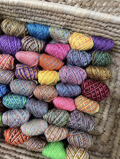 Many colourful balls of variegated yarn stacked in a woven basket