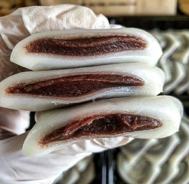 Hand holding three white mochi rice cakes with red bean paste filling visible in cross-section