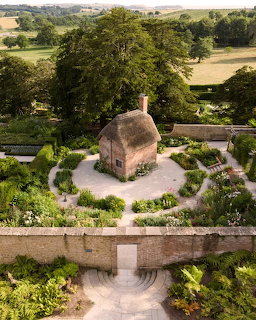 Aerial view of a small thatched cottage inside a formal walled garden with paths and greenery