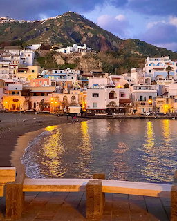 Colorful Italian coastal town at dusk with lit buildings along a harbor and green mountain behind