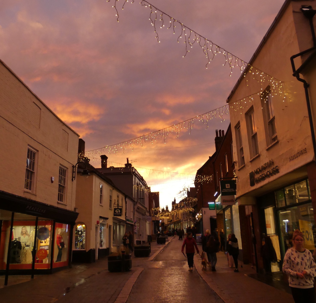Pedestrian shopping street in Woodbridge at sunset with shopfronts and string lights