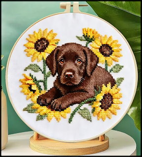 Cross-stitch embroidery of a chocolate Labrador puppy among sunflowers in a wooden hoop