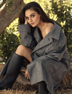 Woman in gray coat and black leather pants sitting outdoors in natural setting
