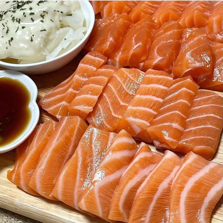 Sliced salmon sashimi on wooden board with soy sauce and white garnish in bowls