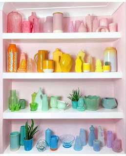 White shelves with colorful vases and decorative objects arranged in rainbow gradient order