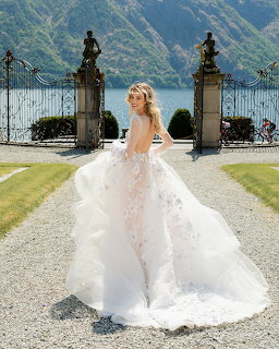 Blonde bride in white ball gown posing on garden path overlooking Lake Como with mountains