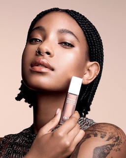 Young woman with braids holding a cosmetic bottle near her cheek in a beauty campaign photo