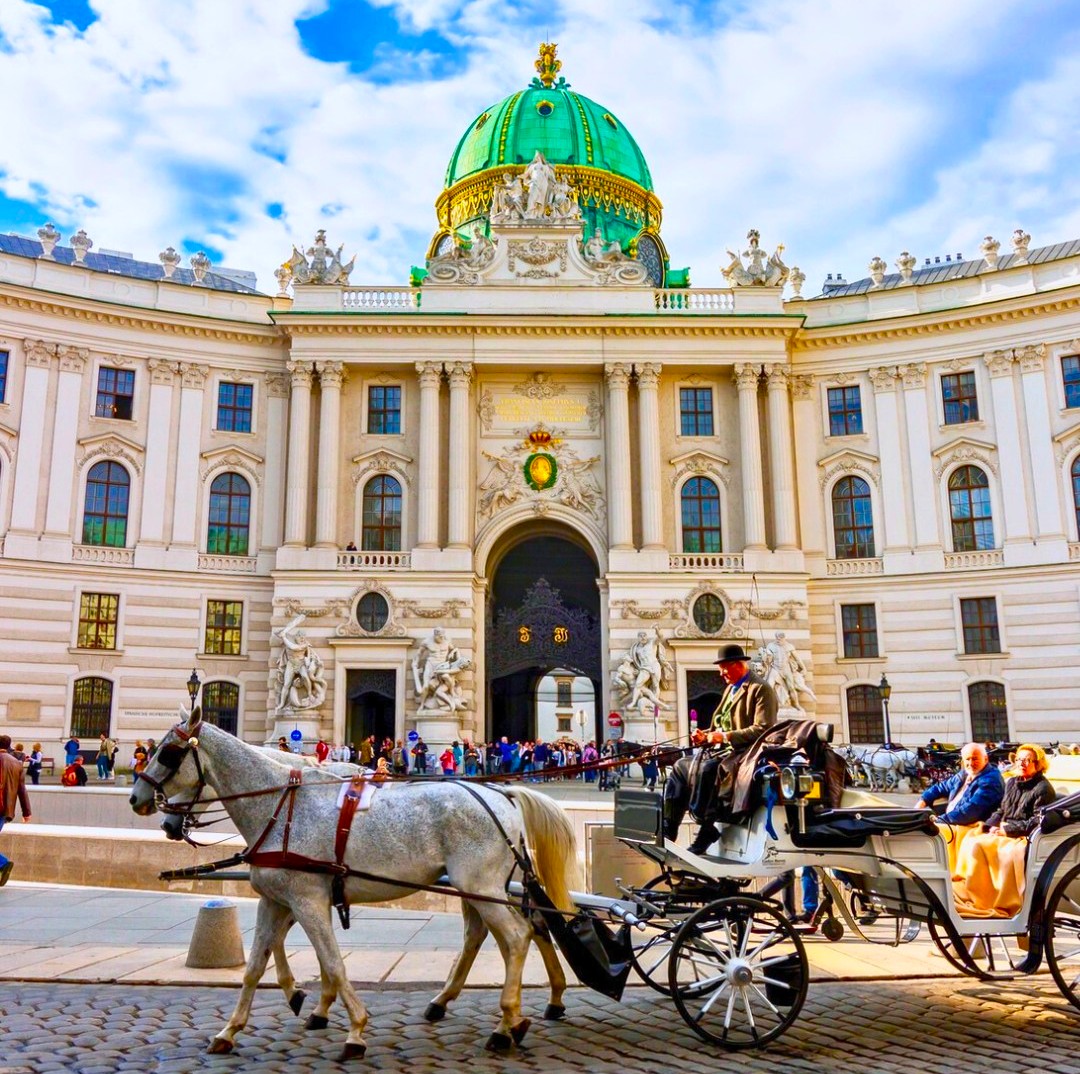 Horse-drawn carriage in front of ornate Hofburg Palace with green dome in Vienna, Austria
