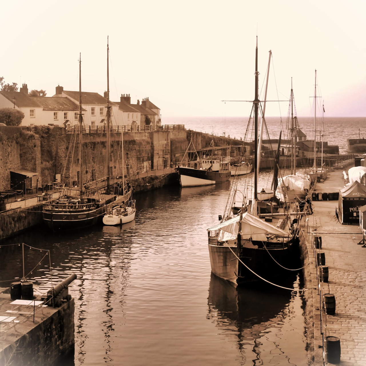 Sepia harbor scene with sailing boats moored beside old stone quays and calm water