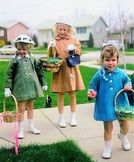 Three young girls in green, tan, and blue coats carrying Easter baskets on a sidewalk