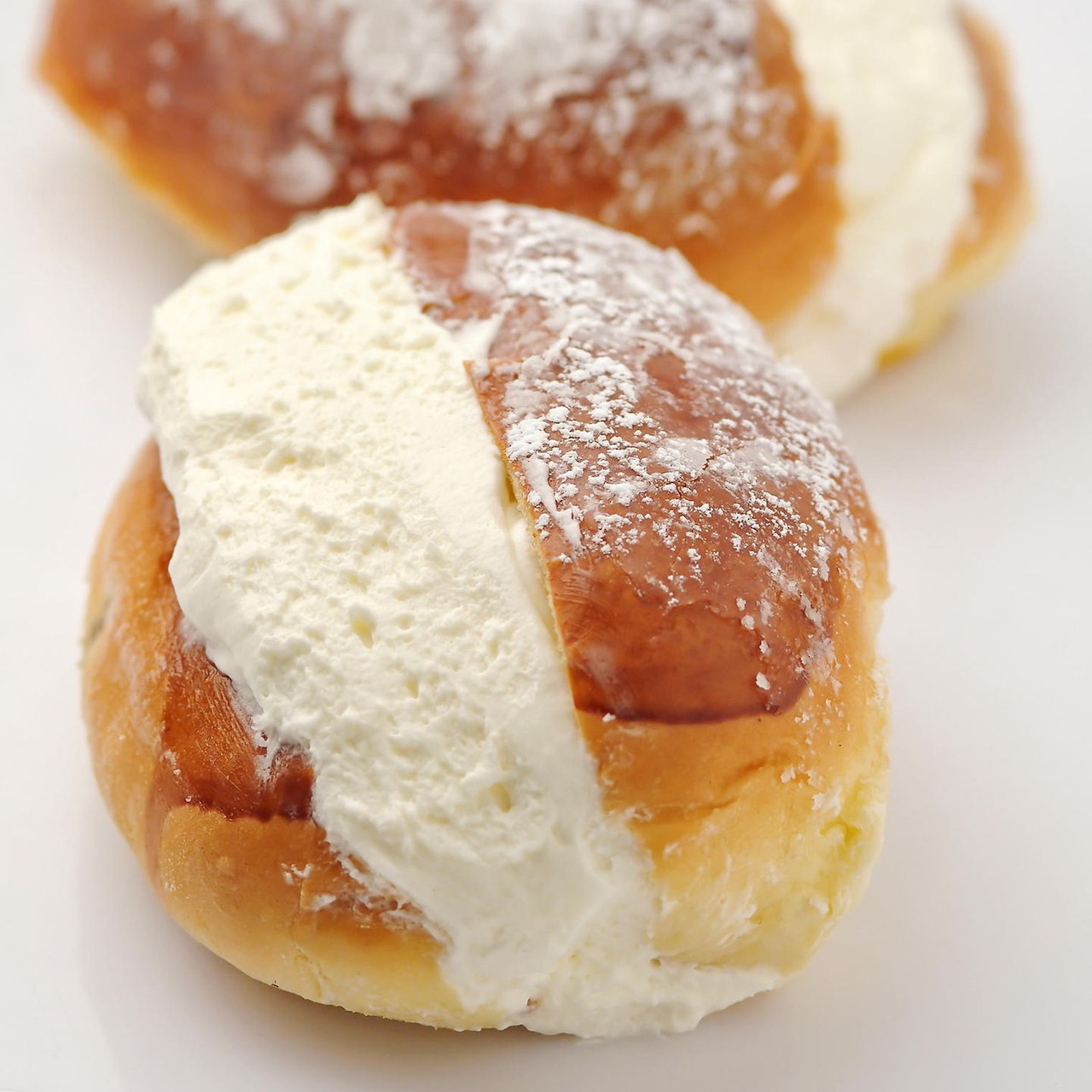 Two cream-filled pastries with powdered sugar on a white background