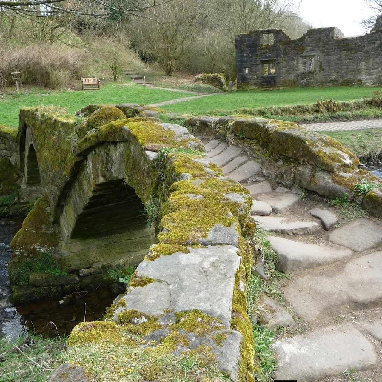 Moss-covered ancient stone bridge with stone steps and ruins in a grassy rural landscape