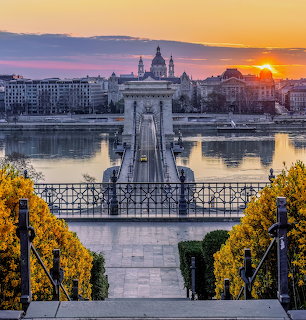 Chain Bridge spanning Danube River in Budapest at sunrise with golden sky and city buildings