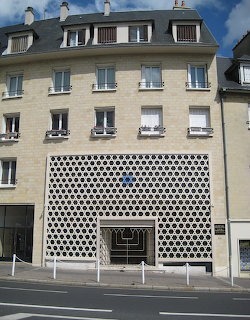 Synagogue in Caen with geometric Star of David pattern facade and cream-colored residential building above