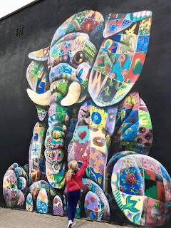 Colorful painted elephant sculpture against a dark wall with a person standing in front