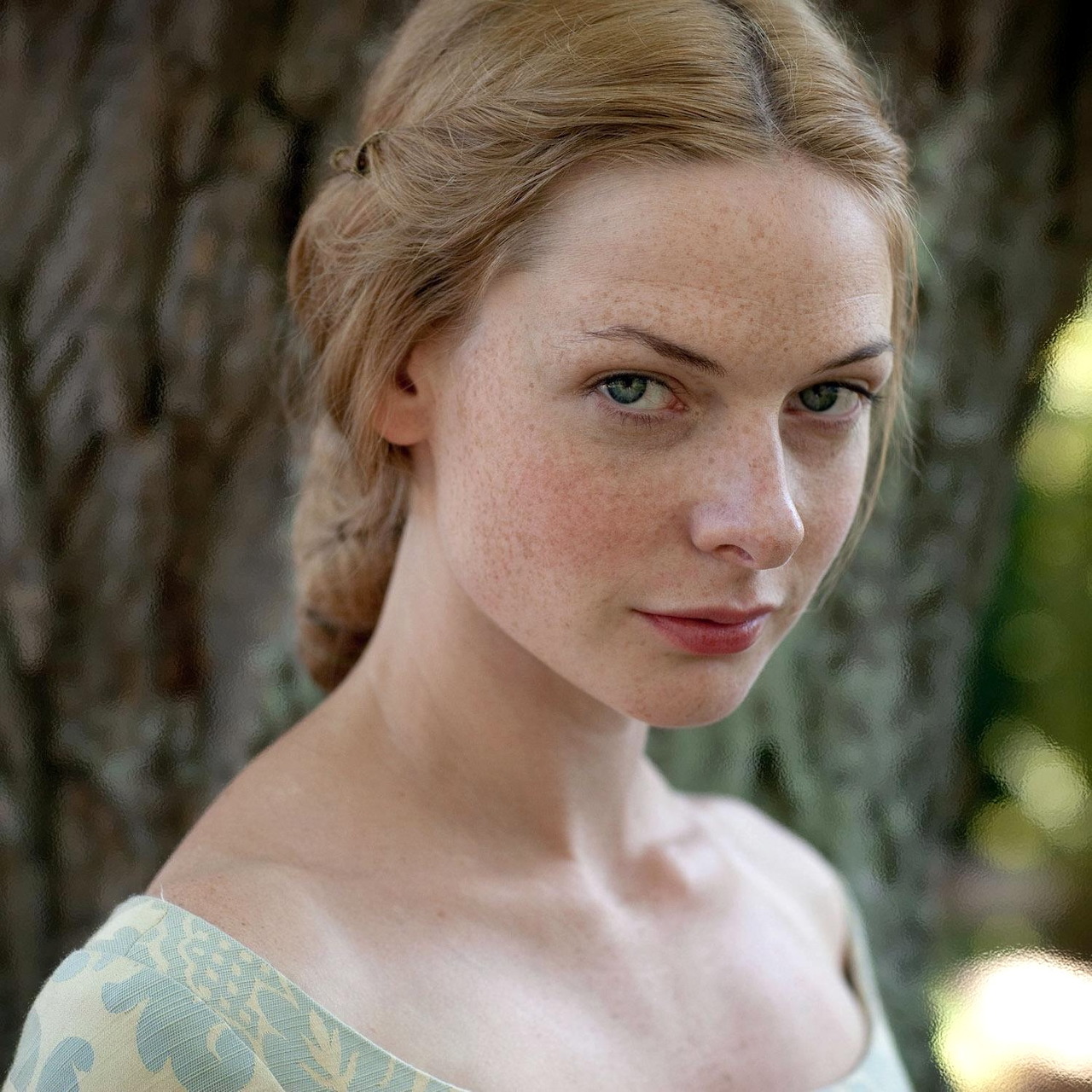 Close-up portrait of a freckled blonde woman beside a tree outdoors