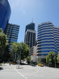 Tall modern skyscrapers and office buildings on a city street with trees under blue sky