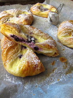 Several golden pastries with blueberry filling dusted with powdered sugar on baking parchment