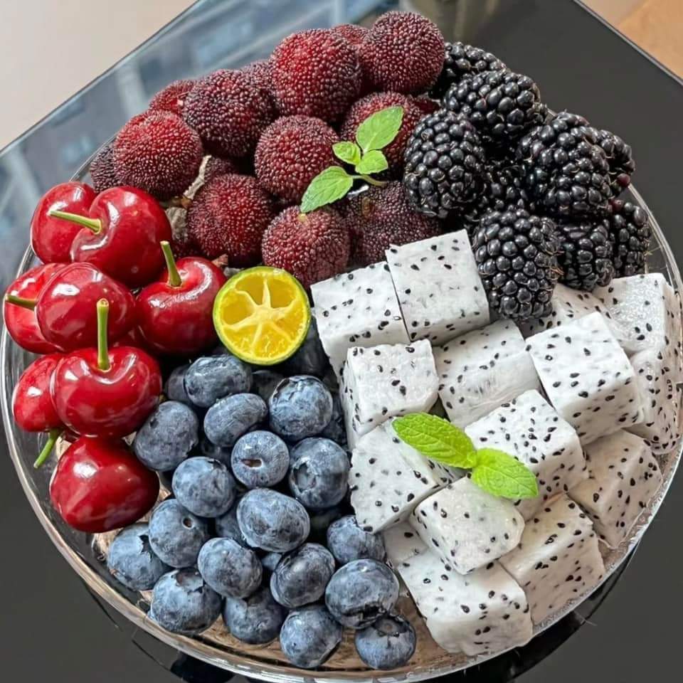 Round platter of assorted fresh fruits including cherries, blueberries, dragon fruit, blackberries, and bayberries