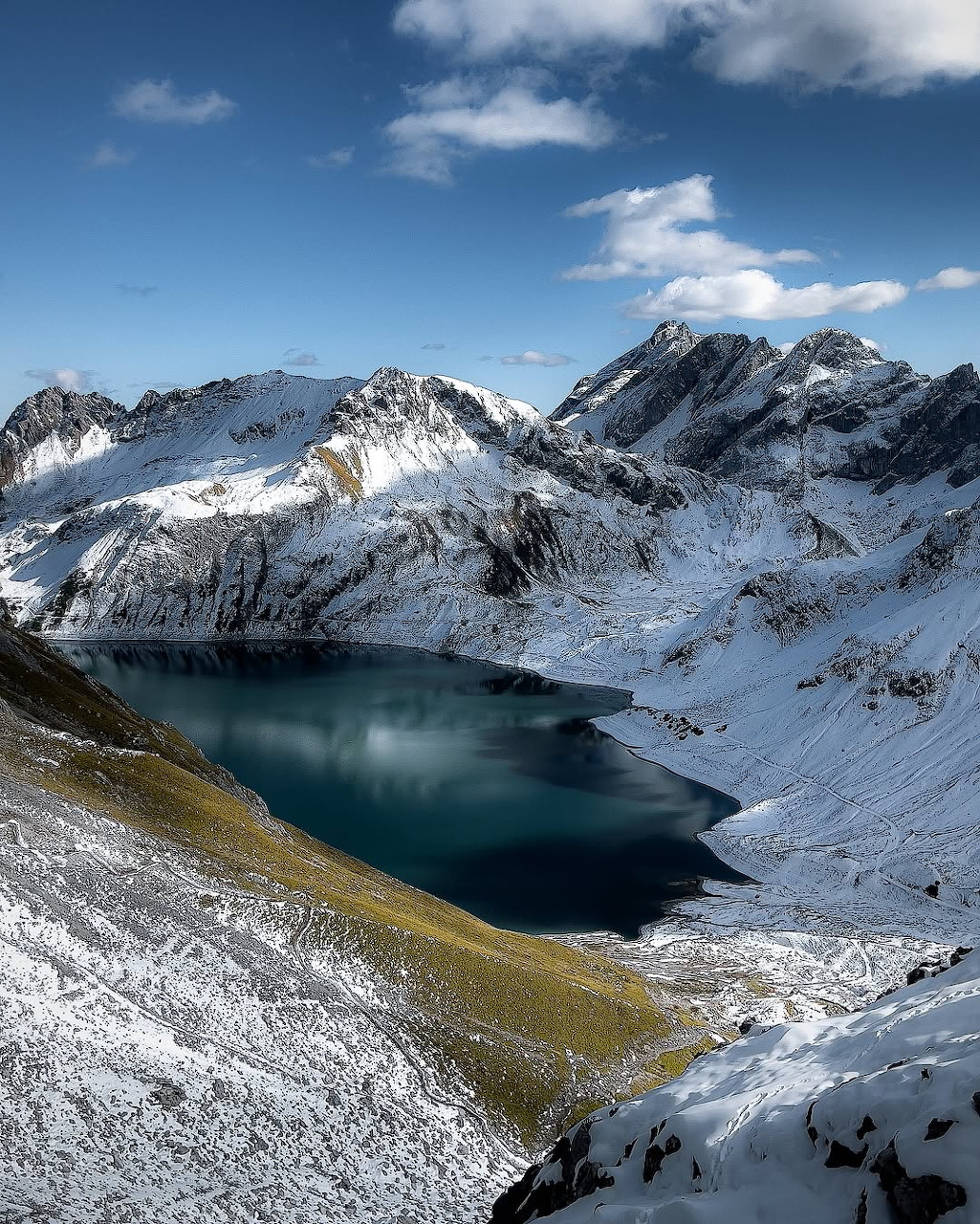 Turquoise alpine lake surrounded by snow-covered mountain peaks and rocky ridges under a blue sky