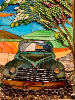 Mosaic artwork of an old green pickup truck beneath a tree against rolling hills