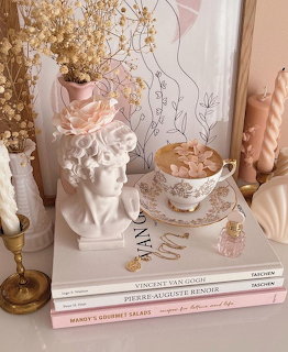 Flat lay of coffee cup on books with dried flowers and white angel statue in soft pink tones