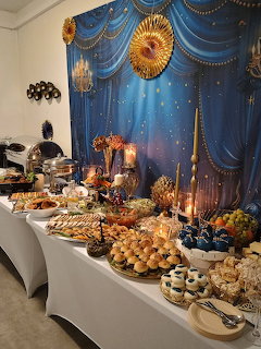 Lavish buffet table with assorted Polish dishes, pastries, and fruits against a blue and gold draped backdrop
