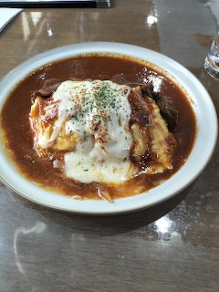 Omurice dish with omelet, white sauce, curry gravy, and garnish in white bowl