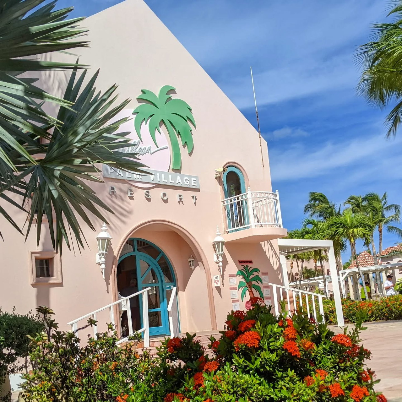 Pink tropical building with palm trees, flowers, and blue sky