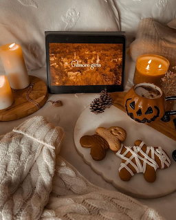 Cozy autumn scene with gingerbread cookies, candles, pumpkin mug, and tablet on a blanket