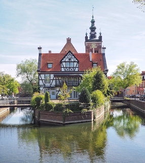 Half-timbered house on a small island surrounded by water with a church tower behind it in Gdansk, Poland