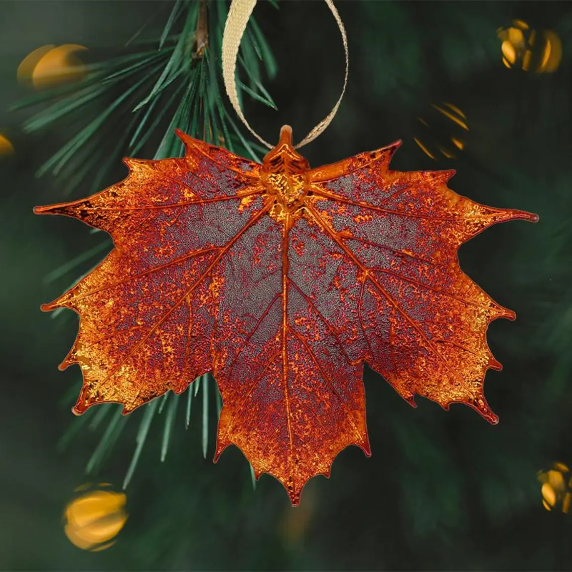 Copper-colored maple leaf ornament with detailed veining hanging on pine branches