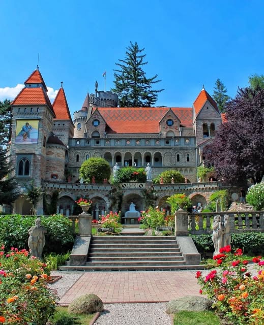 Elegant castle with turrets and gardens featuring fountain, flowerbeds, and manicured lawn
