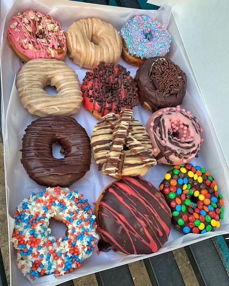 Twelve assorted decorated donuts with various frostings and toppings in a white box