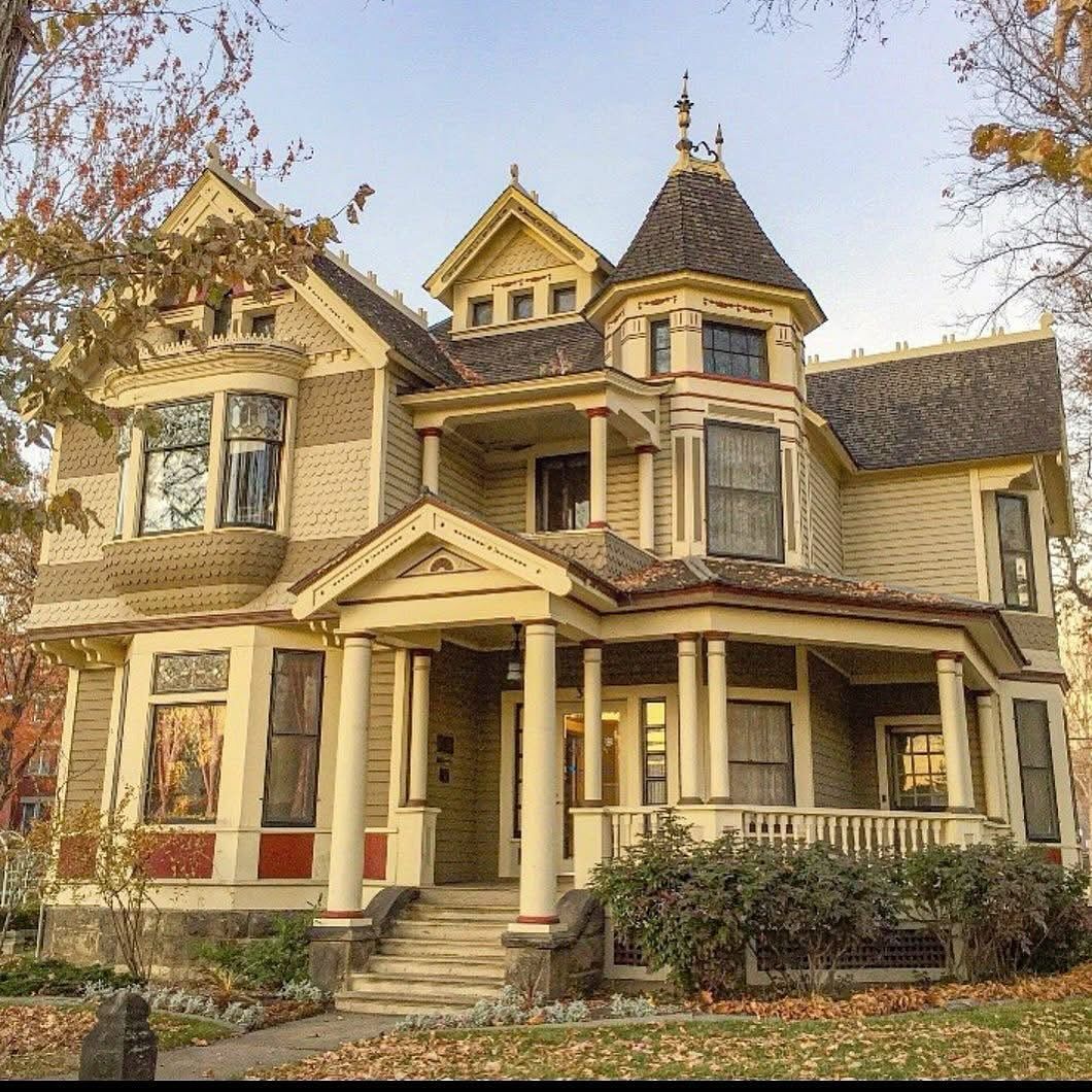 Yellow Victorian house with round turret and decorative trim framed by fall trees