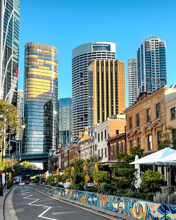 Street in The Rocks, Sydney with historic buildings, colorful wall mural, and modern skyscrapers behind