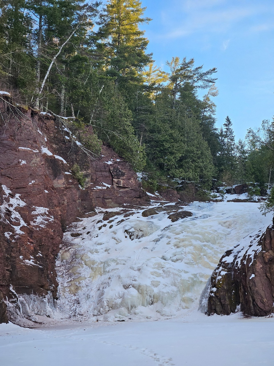 Rushing waterfall cascading over red rock cliffs surrounded by snow and evergreen trees in winter
