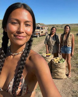 Two Native American women standing on open prairie with burlap sacks of fruits and vegetables