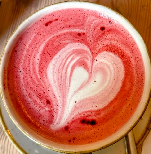 Top view of a pink latte with heart-shaped foam art in a cup on a saucer